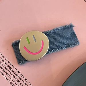 Denim cloth hair clip with smiling face metal badge and fringe edges on pink background