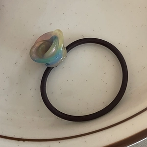 Detail of high-elastic black hair tie with iridescent resin flower charm in ceramic tray