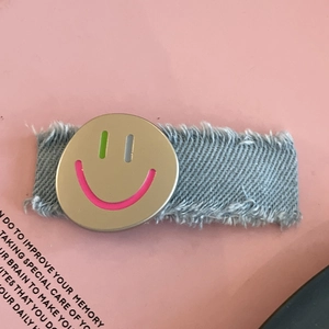 Denim cloth hair clip featuring a golden smiley face with vibrant colorful accents