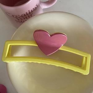 Gros plan d'une pince à cheveux jaune et rose avec cœur sur un bol en céramique