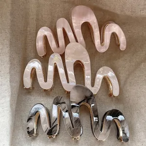 Three wavy acetate claw clips in pink, pearl white and marble grey on beige linen cloth