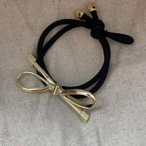 Elegant black elastic hair tie with polished gold metal bow charm on linen background
