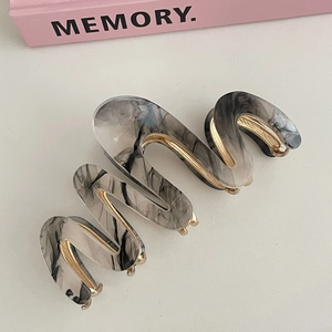 Detail view of wave-shaped grey marble acetate hair claw clip with gold metal frame