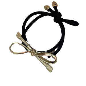 Elastic black hair tie with a minimalist gold metallic bow pendant on white background