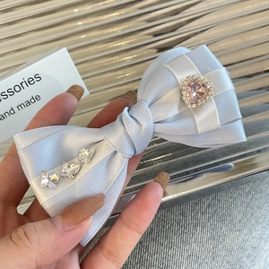 Detail of light blue satin bow hair clip with heart rhinestone held in hand