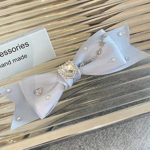 Detail of light blue satin bow hair clip with heart crystal and star pendants