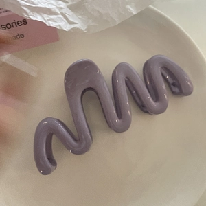 Gros plan d'une grande pince à cheveux ondulée lavande sur une assiette blanche élégante