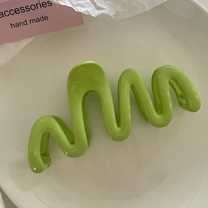 Vue détaillée de la pince à cheveux ondulée vert citron sur un plateau blanc minimaliste
