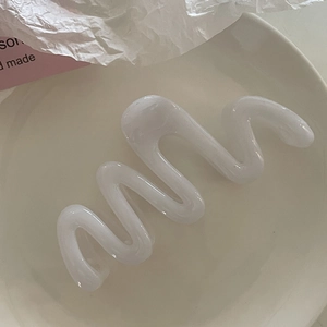Détail macro d'une grande pince à cheveux blanche ondulée translucide sur une assiette en céramique