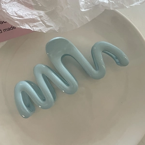 Gros plan d'une grande pince à cheveux bleu clair en forme de vague sur une assiette blanche