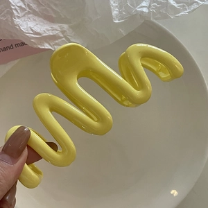 Grosse pince à cheveux ondulée jaune vif, vue rapprochée sur un fond minimaliste chic