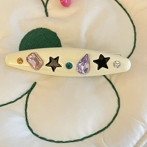 Detailed close-up of a cream hair clip featuring black stars and colorful rhinestones