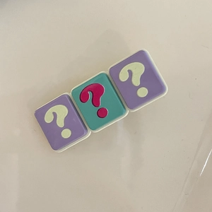 Close-up of a three-block hair clip in purple and green with yellow question marks