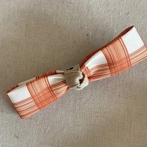 Barrette à nœud à carreaux orange et blanc avec nœud kaki sur fond de lin rustique