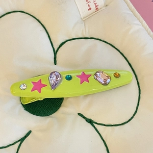 Detail of neon green rhinestone hair clip with pink star on floral fabric background
