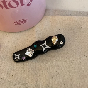 Close-up of wavy black hair clip with colorful rhinestones and white star patterns