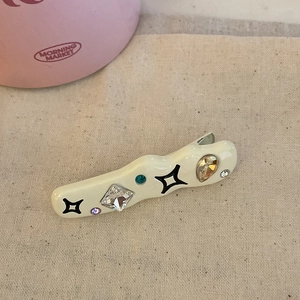 Detail of a wavy cream acetate hair clip with colorful rhinestones and black star patterns