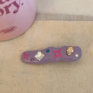 Macro shot of purple wavy hair clip with colorful rhinestones and pink star patterns