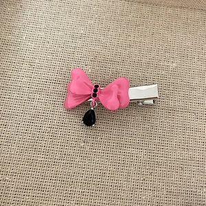 Detailed view of pink enamel bow hair clip with black crystal center and teardrop charm