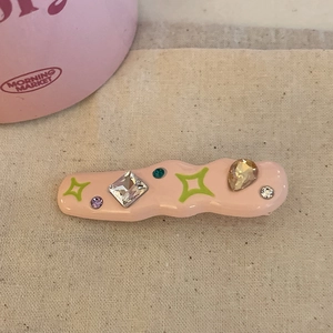 Macro view of pink wavy barrette with colorful rhinestones and star patterns on beige fabric