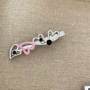 Macro view of silver heart hair clip with pink enamel and black crystal accents