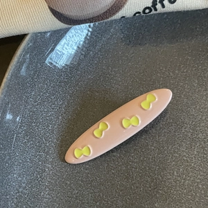 Close-up of a pink resin hair clip with yellow bow patterns on a textured tray