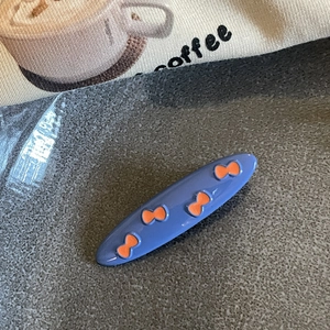 Close-up of a blue oval hair clip with orange bow patterns on a canvas background