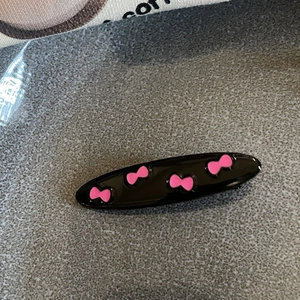 Close-up of a glossy black oval hair clip with four cute pink bow patterns