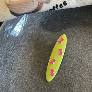 Detailed macro view of a bright green oval hair clip with four pink bow patterns