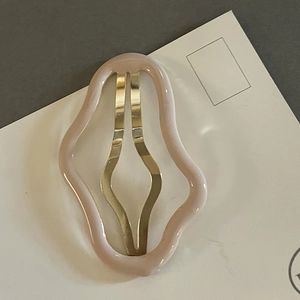 Détail d'une barrette à cheveux rose ondulée avec base en métal doré sur carte support