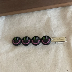 Détail d'une pince à cheveux argentée avec quatre smileys noirs et gravure fait main