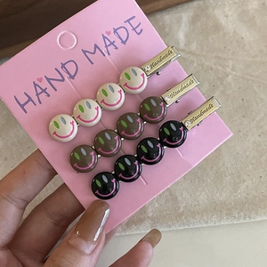 Trois barrettes à cheveux smiley colorées en métal beige, marron et noir sur une carte