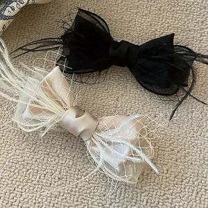 Detail of luxury bow hair clips featuring black and champagne satin with mesh and feathers