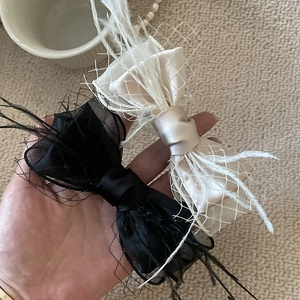 Elegant black and champagne bow hair clip with feathers and mesh layers held in hand