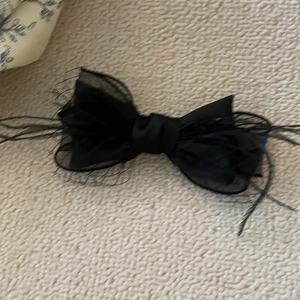 Exquisite black layered mesh bow hair clip with feather accents on a textured beige surface