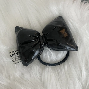 Glossy black leather bow hair tie with stylish white label on a soft white fur backdrop