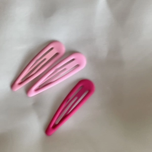 Détail de trois barrettes à cheveux roses mates sur un tissu blanc froissé