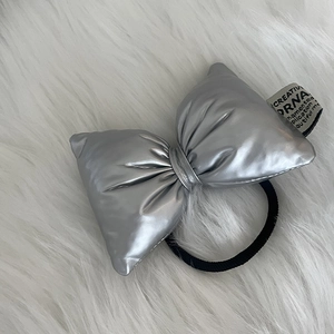 Silver metallic bow hair tie with puffy 3D texture and black elastic on white faux fur