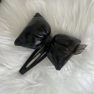 Close-up of a glossy black leather bow hair clip with a metallic BB clip on white fur