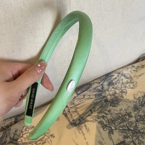 Detailed shot of light green satin padded headband with silver tag and handmade label