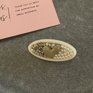 Vue détaillée de la pince à cheveux ovale avec cœur brun, résine crème, perles et strass