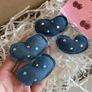 Gros plan de quatre pinces à cheveux coeur en denim avec strass colorés en boîte