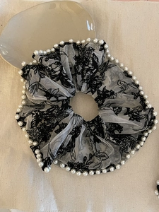 Macro detail of large white mesh hair scrunchie with black floral embroidery and pearl trim