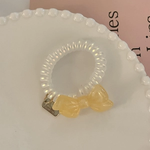 Elegant spiral hair tie with a soft yellow resin bow on a clean ceramic display
