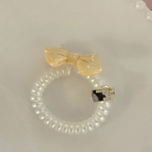 Pearlescent spiral hair tie with a cream resin bow and tiny metal logo charm