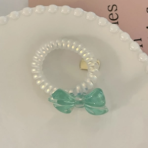 Macro shot of a mint green bow hair tie and spiral band on a white pearl plate