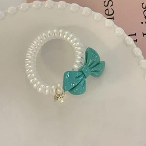 Close-up of cream spiral telephone cord hair tie with a teal resin bow charm on a tray