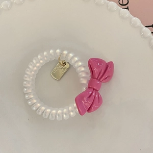 Detail of pearl white spiral hair tie with a pink bow and golden metal tag charm