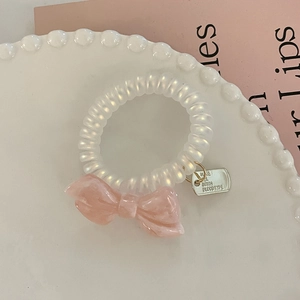 Detail of pearlescent hair tie with pink marble resin bow and metal tag in a ceramic tray