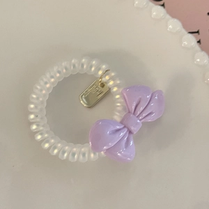 Close-up of spiral hair coil with purple bow and gold metal tag on white plate